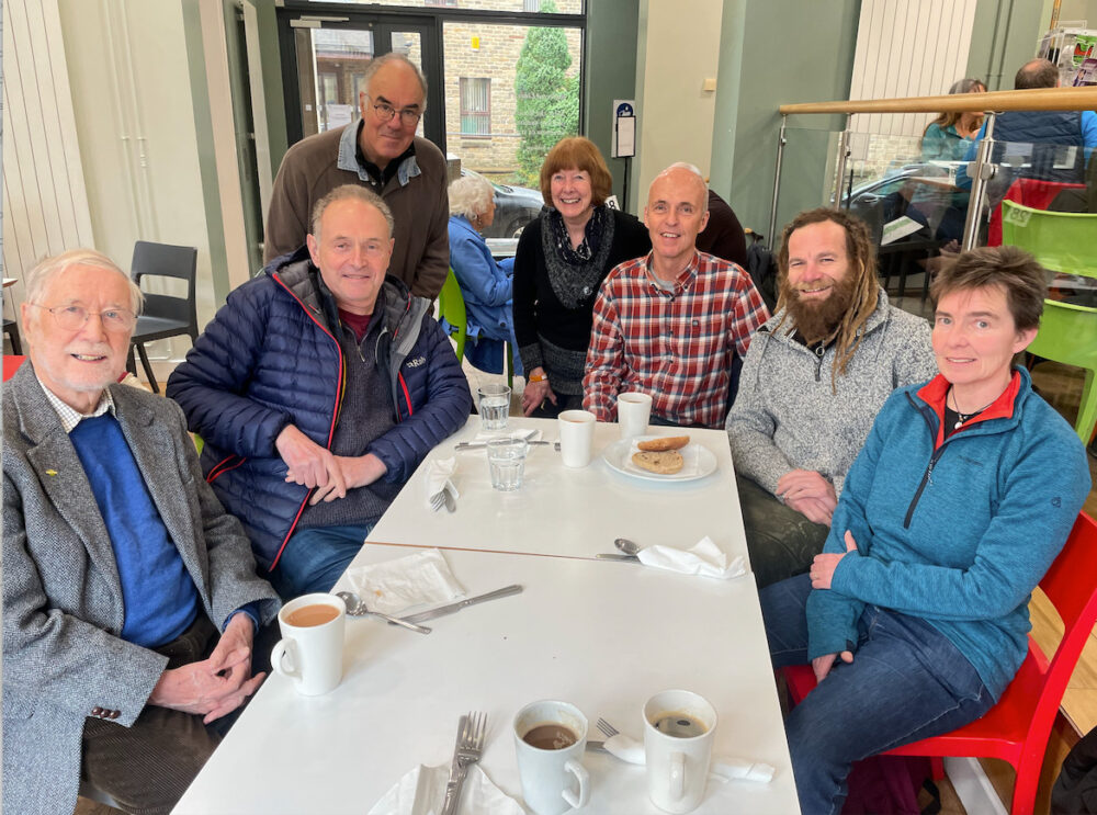in the canteen at Hebden Bridge town hall. All seven original members of Gritstone sitting around dining table during lunch, all looking at camera)