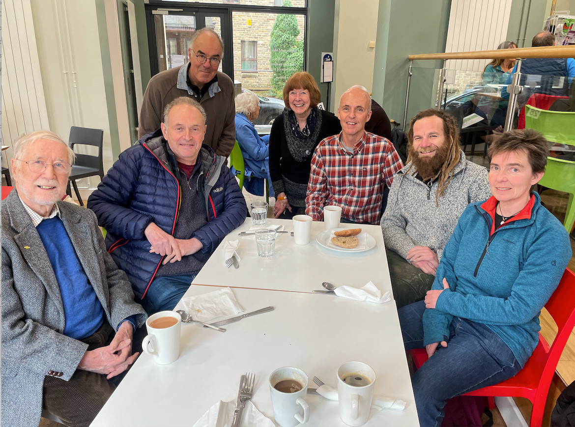 in the canteen at Hebden Bridge town hall. All seven members (at the time) of Gritstone sitting around dining table during lunch, all looking at camera