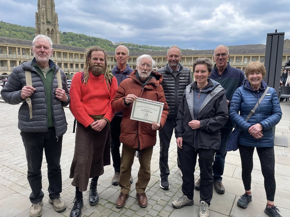 Image of Colin holding award certificate surrounded by members of Gritstone Cooperative in the courtyard of the Piece Hall